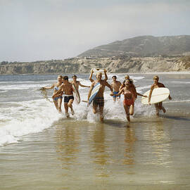 Group Of Surfers Running In Water With by Tom Kelley Archive